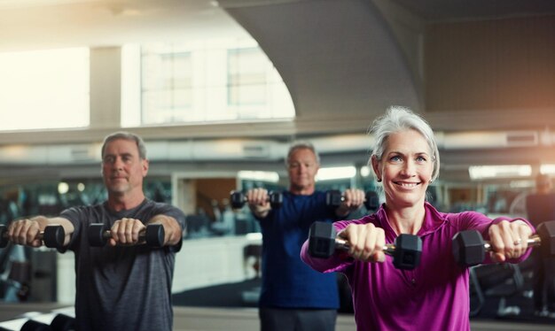 Foto dumbbells do clube de fitness sênior e pessoas no ginásio para treinamento de saúde e bem-estar, esporte ou exercício. exercício de classe e grupo de amigos idosos em um estúdio para cardio com peso manual ou levantamento de pesos.