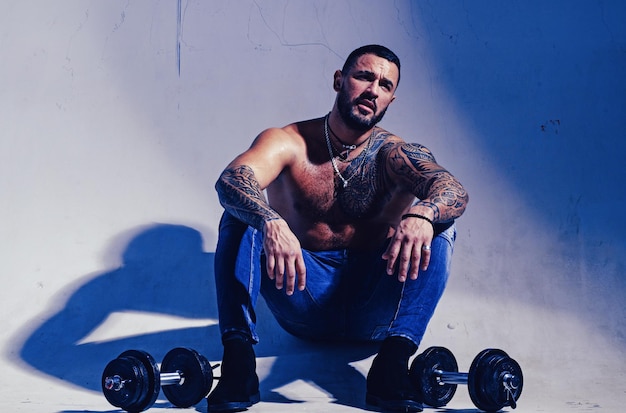 Dumbell hebt sexy Bauchmuskeln von Tattoo-Mann männliche Mode muskulöser Macho-Mann mit athletischem Körper brutal spo