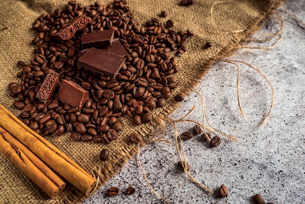 Dunkel geröstete aromatische Kaffeebohnen dunkle und poröse Schokoladen-Zimtstangen auf einem braunen Tuch 2