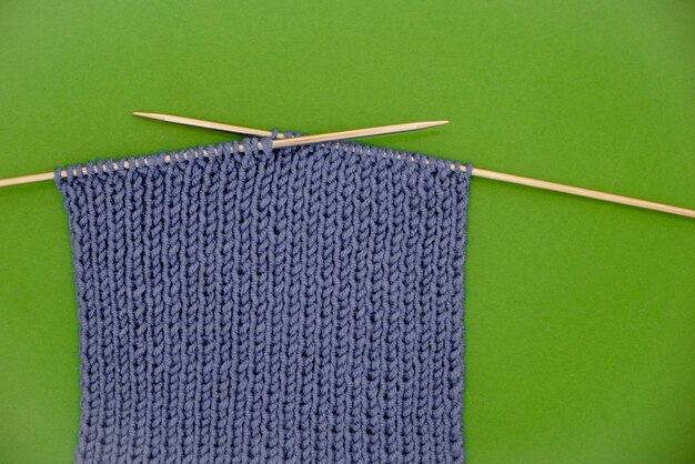 Dunkelgrauer gestrickter Schal mit grünem Hintergrund der Stricknadeln.