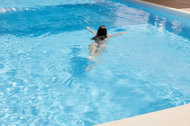 Dunkelhaarige Frau mit Badeanzug, die auf blauem Wasserpool im Luxus-Spa-Salon oder im Hotel schwimmt, Freizeit verbringt und ihre Sommerferien im Schwimmbad genießt. Urlaub, Entspannung, Ruhekonzept.