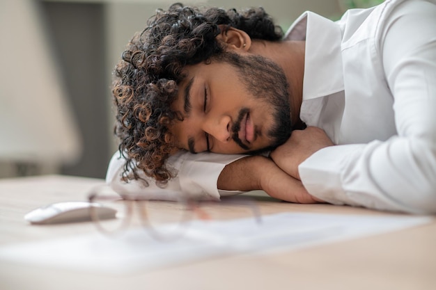 Dunkelhaariger geschäftsmann, der am tisch sitzt und ein nickerchen macht