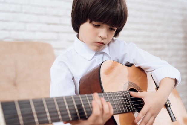 Dunkelhaariger Junge in einem weißen Hemd spielt die Gitarre.