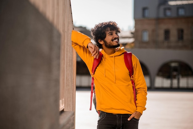 Dunkelhaariger junger Mann in orangefarbenem Hoodie mit Rucksack