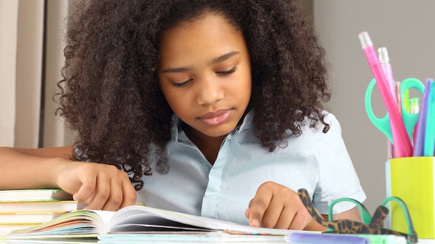 Dunkelhäutiges Schulmädchen, das ein Buch liest und Hausaufgaben macht