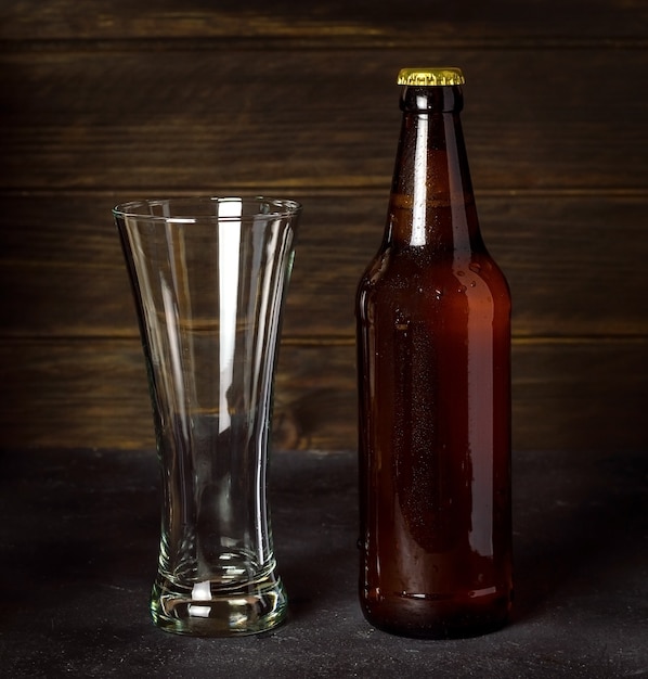 Dunkle Bierflasche mit leerem Glas auf dunklem Holz.