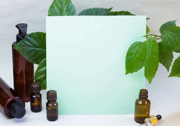Dunkle kosmetische Flaschen und grüne natürliche Blätter auf einem hellen Hintergrund