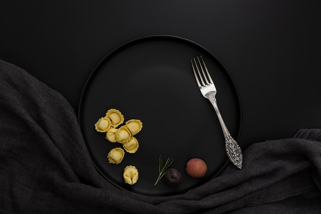 Foto dunkle platte mit tortellini und gabel auf einem schwarzen hintergrund