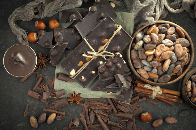 Foto dunkle schokolade in einer zusammensetzung mit kakaobohnen und nüssen, auf einem alten hintergrund.