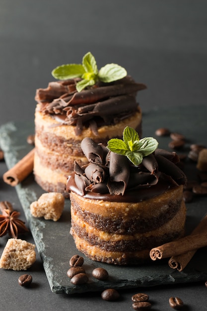 Dunkle Schokoladenkuchen auf schwarzem slattern Brett mit Minze, Zimt, Kaffeebohnen auf einem hölzernen Hintergrund. Tasty Dessert Food-Konzept.