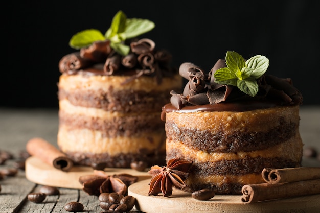 Dunkle Schokoladenkuchen auf schwarzem slattern Brett mit Minze, Zimt, Kaffeebohnen auf einem hölzernen Hintergrund. Tasty Dessert Food-Konzept.