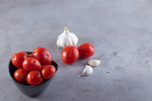 Dunkle Schüssel mit eingelegten Tomaten auf Steintisch gelegt.