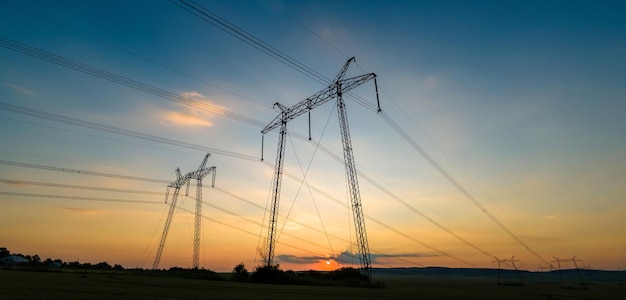 Dunkle Silhouette von Hochspannungstürmen mit Stromleitungen bei Sonnenaufgang