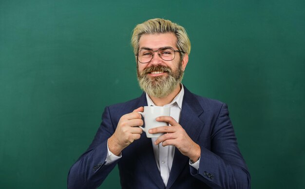 Dunkler Kaffee, strahlende Zukunft. Glücklicher Lehrer hält Kaffeetasse. Bärtiger Mann trinkt gerne Kaffee. Kaffeepause. Schulpause. Ausruhen und Entspannen. Inspirierte Kreativität.