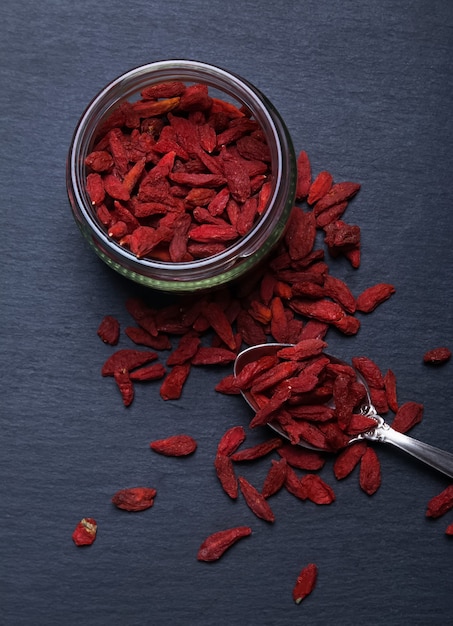 Dunkles Artfoto von Goji-Beeren in einem Glas auf einem schwarzen Hintergrund, Draufsicht