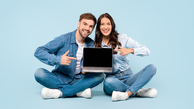 Foto un dúo sonriente en denim con una computadora portátil apuntando a la pantalla