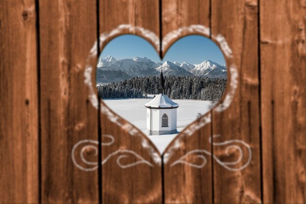 Foto durch ein geschnitztes herz in einer holzwand zu einer romantischen kapelle im winter schauen