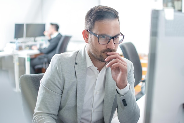 Durch Glasblick auf einen hübschen, besorgten Mann in Geschäftsbekleidung, der an einem Computer in einem hellen Büro arbeitet