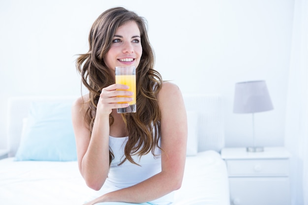 Durchdachter Brunette, der ein Glas Orangensaft trinkt