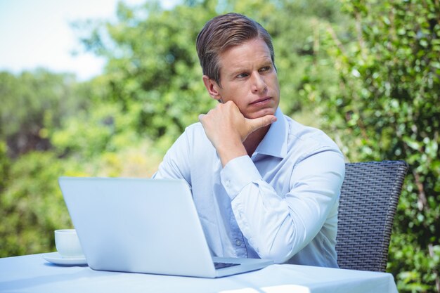 Durchdachter Geschäftsmann unter Verwendung des Laptops mit Kaffee