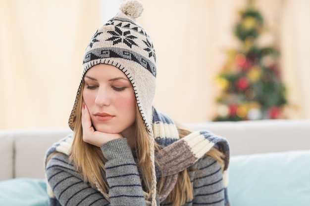 Durchdachter hübscher Brunette mit dem Winterhut, der auf Couch sitzt