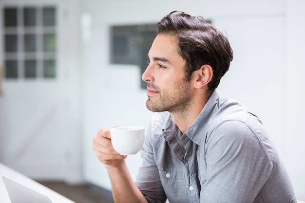 Durchdachter junger Mann, der Kaffeetasse hält