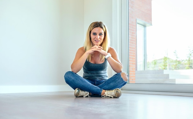 Durchdachtes blondes Mädchen, das in einem leeren Wohnzimmer sitzt