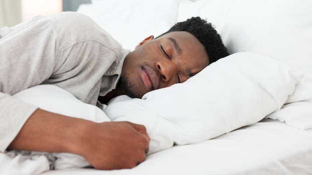 Durma, relaxe e sonhe para um homem negro em casa na cama em uma manhã de fim de semana Cansado de dormir e sonhar sozinho no quarto Paz relaxante e conforto com a cabeça no travesseiro para dormir em um quarto iluminado