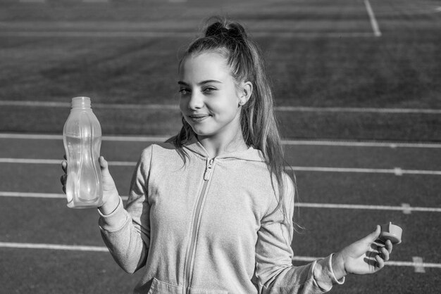 Durstiges und hydratisierendes Teenager-Mädchen trinkt Wasser im Stadion Kind in Sportkleidung entspannt sich im Freien Kind trainiert auf der Rennstrecke gesundes Kindheitstraining an der frischen Luft im Freien