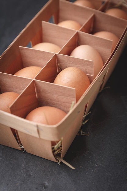 Dúzia de ovos de galinha marrom em uma caixa de madeira compensada em um fundo de ardósia preta