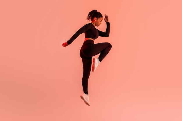 Dynamische Bewegungen bestimmen die schwarze Dame, die Ellbogen-Knie-Crunches macht oder auf rotem Neon springt