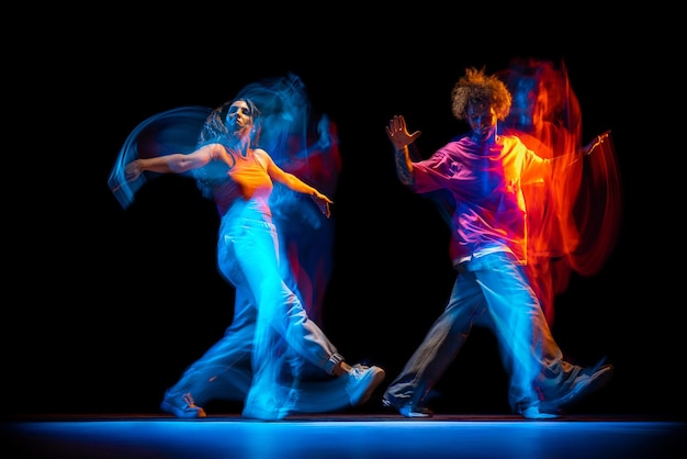 Dynamisches Porträt eines jungen Mannes und einer Frau, die Hiphop tanzen, isoliert auf schwarzem Hintergrund mit gemischtem Lichteffekt