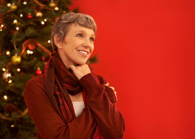 Foto É a estação para ser alegre uma mulher madura feliz olhando pensativa na frente de uma árvore de natal