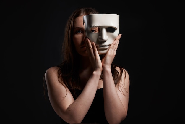 Foto É a única maneira de me encaixar. foto de estúdio de uma mulher se escondendo atrás de uma máscara em branco.