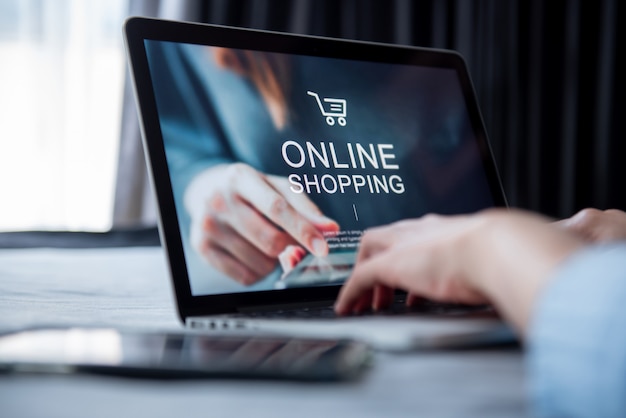 E-commerce e conceito de compras on-line, mão de mulher usando laptop (site de maquete) e segurando o cartão de crédito para fazer compras de pagamento on-line em casa.