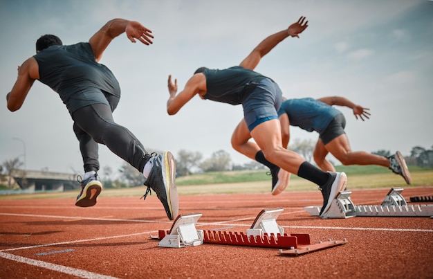 E eles estão desligados. Tiro retrovisor de três jovens atletas masculinos irreconhecíveis começando sua corrida em uma pista.