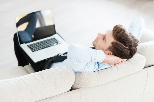 É hora de fazer uma pausa. Vista superior do jovem empresário segurando laptop nas pernas