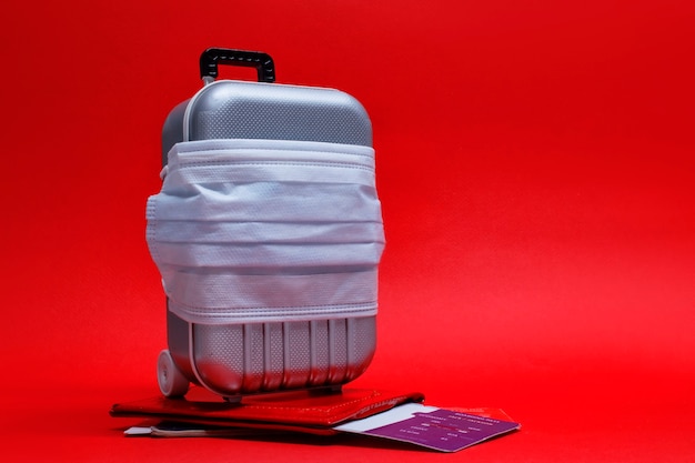 É hora de viajar. Cancelamento de voo e conceito de descanso seguro durante uma pandemia de Covid-19 Coronavirus. Mala de viagem com máscara médica e passagem aérea com passaporte.