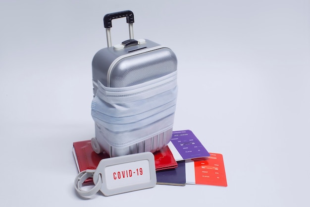 É hora de viajar. O conceito de descanso seguro durante uma pandemia de Covid-19 Coronavirus. Mala de viagem com máscara médica e passagem aérea com passaporte.