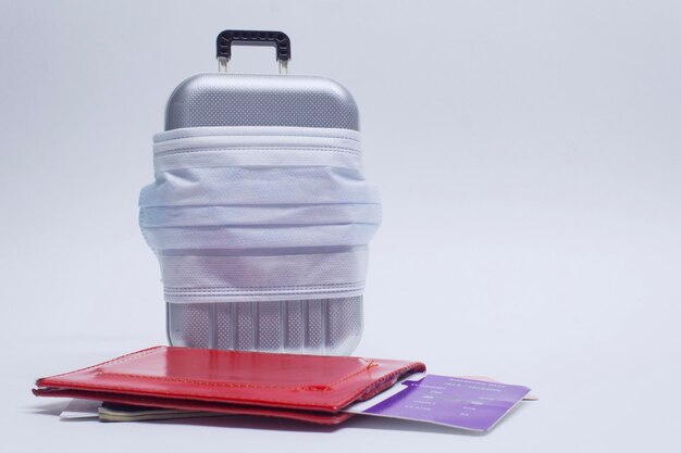 É hora de viajar. O conceito de descanso seguro durante uma pandemia de Covid-19 Coronavirus. Mala de viagem com máscara médica e passagem aérea com passaporte.