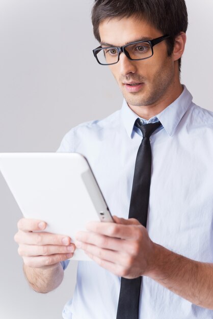 É simplesmente incrível! Jovem surpreso de camisa e gravata olhando para tablet digital