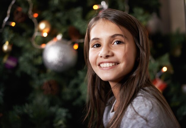 É uma época alegre do ano foto de uma garotinha sentada perto de uma árvore de natal