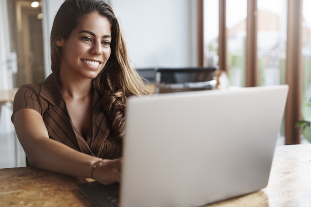 e uma mulher hispânica de sucesso sorrindo usando laptop no café