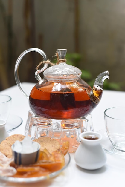 Earl Grey Tee in Teekanne aus Glas mit Tassen und kristallisierten Früchten auf weißem Hintergrund