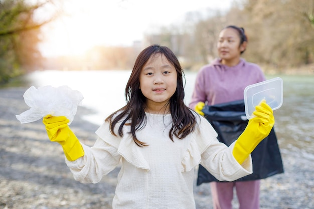 Earth Day-Konzept Frau und Tochter holen Müll in Müllsäcken auf, reinigen in der Natur, um in ihren Gemeinden saubere Flüsse zu recyceln und die Umwelt vor Verschmutzung zu schützen Natur
