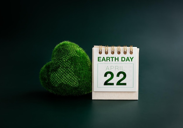 Earth Day Konzept Tag der Erde 22. April Text auf der Datumsseite auf dem Tischkalender in der Nähe von grünem Gras Herzball mit Weltkarte auf dunkelgrünem Hintergrund Umwelt und Planetenschutz Happy Earth Day