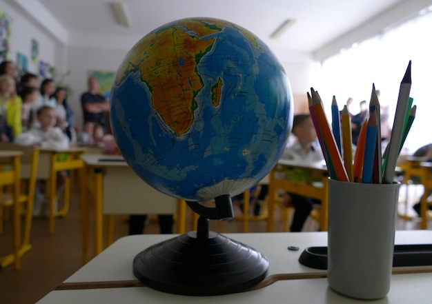 Earth Globe und Buntstifte auf dem Schreibtisch neben der Tafel vor den Schulkindern