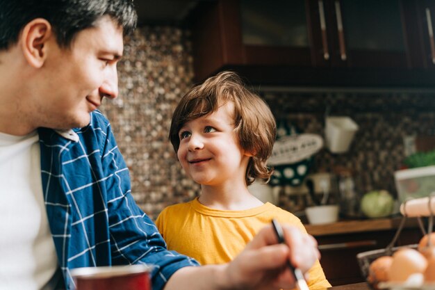 Foto easter-tag männlicher vater und sohn malen eier auf hölzern hintergrund familie sitzt in einer küche