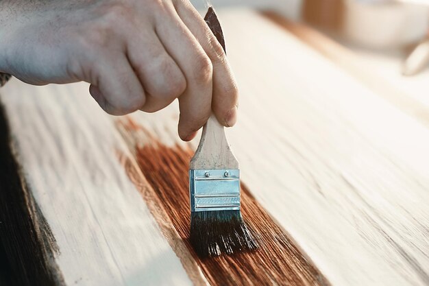 Un ebanista que trabaja sostiene un pincel en la mano y pinta una superficie de madera Un rastro de pintura en una tabla de madera