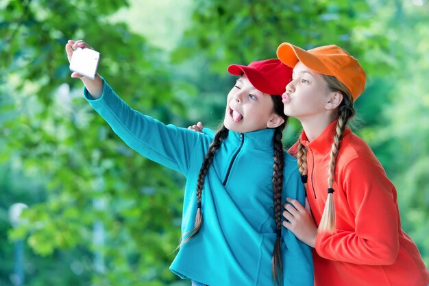 Echar un vistazo Los niños divertidos toman selfie juntos Selfie disparando con un teléfono inteligente Dispositivo móvil Tecnología moderna Videollamada Redes sociales Naturaleza informal